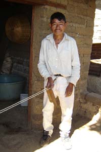 Pablo spins a device in his hand round and round to twist two lengths of spun maguey into a stronger cord.  His wife María holds the center of the maguey lengths as they twist.  Photo by Denise Gallinetti 2005.