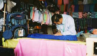 Unfinished hand woven huipiles or Maya blouses are also sold in local markets.  Here a tailor is cutting out the neck of a three-panel piece. To complete the garment, the neck is hemmed and the sides are sewn up. Photo by Margot Blum Schevill 2005.